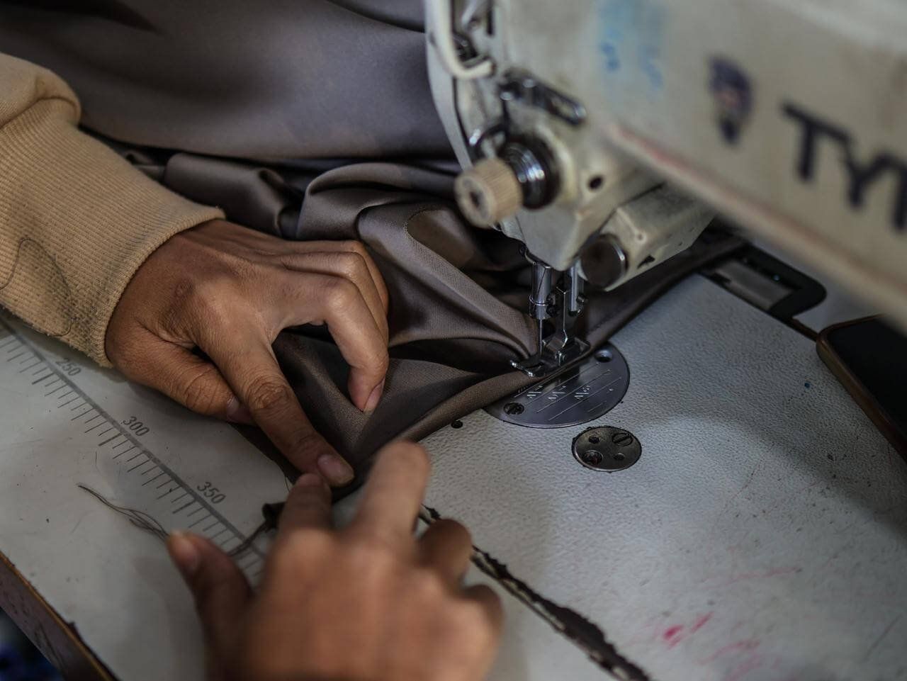 Close up of hands sewing a silk Sampot skirt using an industrial sewing machine.